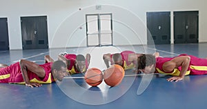 Diverse basketball players perform push-ups in a gym