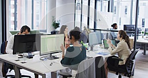 Diverse business colleagues at desks talking using phone headsets and computers in busy office