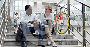 Diverse business colleagues sitting on stairs and talking outside business center