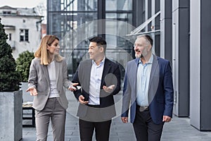 Diverse business group, three male and female workers walking and chatting discussing plans