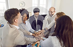 Diverse business people men and women putting their arms together sitting in a circle in office.