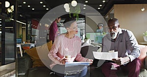 Diverse business people sitting with documents and discussing work at office