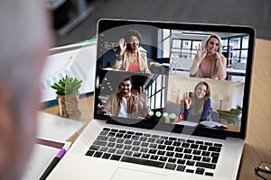 Diverse business people waving displayed on laptop screen during office video call