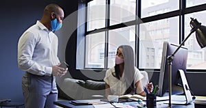 Diverse business people wearing face masks using computer talking in office