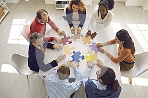 Diverse business team sitting around office table and trying to fit jigsaw pieces together