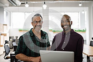 Diverse businessmen smiling and using a laptop in an office