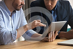 Diverse businessmen talking using digital tablet sit at desk, closeup