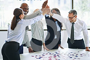 Diverse businesspeople high fiving while solving a jigsaw puzzle