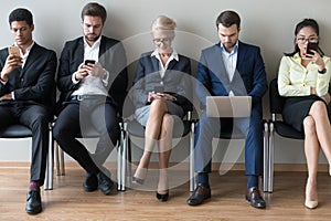 Diverse businesspeople sitting in row using devices phones and laptop