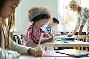 Diverse classmates doing task at lesson studying in classroom with teacher.