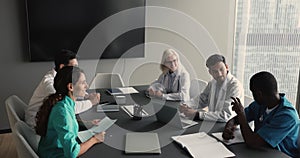 Diverse clinic staff talking at meeting table, discussing teamwork