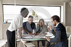 Diverse colleagues consider company paperwork at team office meeting