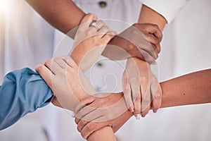Diverse colleagues hands holding wrists from above in support of unity, loyalty and teamwork in the workplace