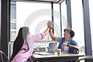 Diverse colleagues high-fiving at table with a laptop in a modern business office photo