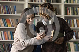 Diverse couple of happy classmates, college students using smartphone