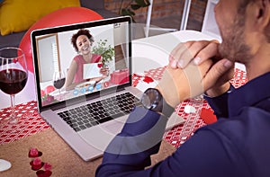Diverse couple making valentine's date video call the woman on laptop screen holding valentine card