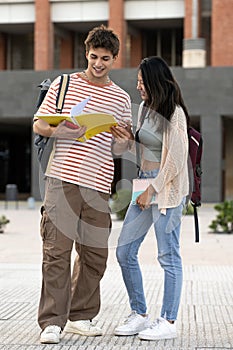Diverse couple standing and reading notes in a campus. Two young students looking notebook smiling and studying in the