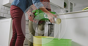 Diverse couple wearing shirt and jacket segregating waste in kitchen