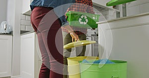 Diverse couple wearing shirt and jacket segregating waste in kitchen