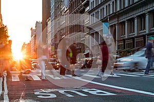 Diverse crowd of people walking across a busy intersection on 23rd Street and 5th Avenue in New York City with sunlight shining