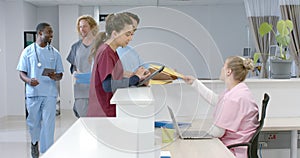 Diverse doctors talking to medical recepcionist sitting at front desk at hospital, slow motion