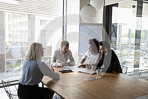 Diverse employees brainstorm discussing paperwork at meeting in office