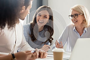 Diverse employees laugh talking sitting at desk in office