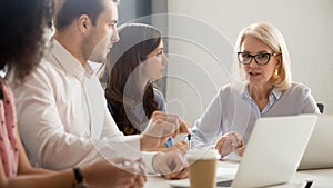 Diverse employees listening to serious mature team leader at meeting