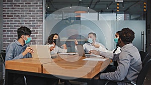 Diverse employees in medical masks quarrel sitting in office angry colleagues arguing group dissatisfied with teamwork
