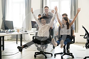 Diverse excited workers having fun riding on chairs on friday