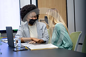 Diverse female business colleagues wearing masks laughing in meeting room