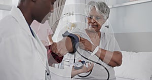 Diverse female doctor taking blood pressure of happy senior female patient in hospital, slow motion