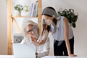 Diverse female employee discuss ideas cooperating using laptop