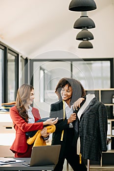 Diverse female fashion designers at work with tailor centimeters on necks and holds tablet and smartphone. independent creative