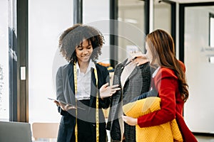 Diverse female fashion designers at work with tailor centimeters on necks and holds tablet and smartphone. independent creative