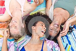 Diverse female friends are lying down, heads together, laughing joyfully