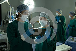 Diverse female and male surgeon in discussion, using tablet in operating theatre during operation