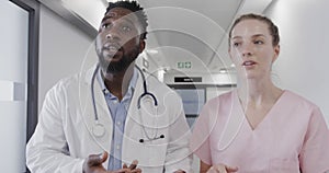 Diverse female nurse and male doctor talking in corridor then running urgently, slow motion