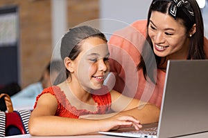 Diverse female teacher and schoolgirl using laptop in elementary school class
