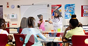 Diverse female teacher and schoolgirls with chemistry items and liquids in elementary school class