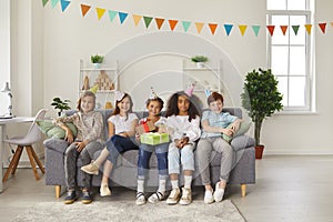 Diverse friends and birthday girl sitting on sofa and smiling for group photo at fun party at home