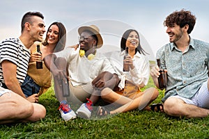 Diverse friends enjoying time outdoors. Multiracial young people having fun together drinking beer and laughing outdoors