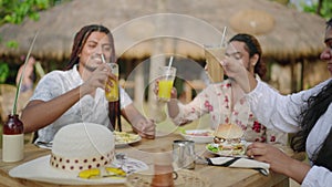 Diverse friends gather, clinking drinks at a tropical outdoor eatery, smiling in a toast to friendship and inclusion