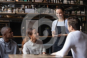 Diverse friends sitting in restaurant placing order talking with waitress
