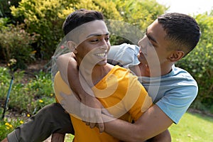 Diverse gay male couple spending time in garden embracing and smiling