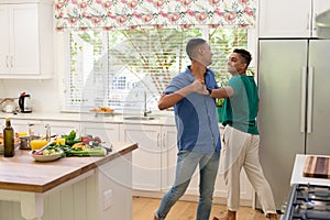 Diverse gay male couple spending time in kitchen dancing