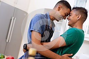 Diverse gay male couple spending time in kitchen embracing and smiling