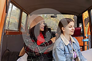 Diverse girlfriends sitting on car trunk in forest and spending time together during road trip