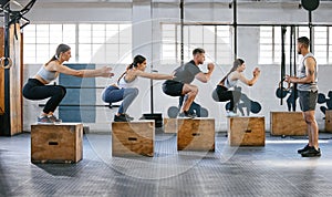 Diverse group of active young people doing box jump exercises together with a trainer in a gym. Focused athletes landing