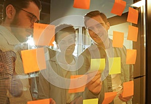 Diverse group of businesspeople standing in an office brainstorming together with sticky notes on a glass wall
